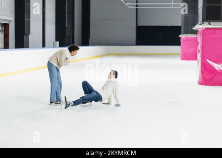 Vista lateral de un hombre cayendo sobre el hielo cerca de una novia afroamericana en la pista de aterrizaje Foto de stock