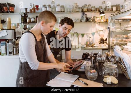 Propietarios masculinos y femeninos haciendo inventario usando tablet PC en el café Foto de stock