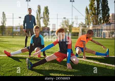 Jóvenes futbolistas haciendo ejercicio de calentamiento estirando las  piernas en el entrenamiento de fútbol. chicos atletas haciendo ejercicio en  el campo antes del partido