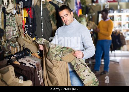 El tipo que elige el uniforme de camuflaje en la tienda militar Fotografía  de stock - Alamy