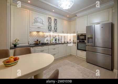 Cocina de estilo minimalista se puede ver un pequeño refrigerador blanco  junto a una ventana, una mesa de comedor con asientos blancos, estantes para  vajilla y una habitación vacía