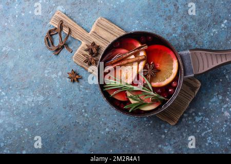 Bebida tradicional de otoño o invierno con naranjas, arándanos, canela, romero y otros ingredientes sobre fondo de hormigón azul Foto de stock