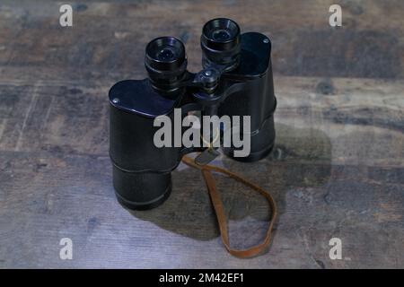 Viejos binoculares militares con arañazos y arañazos del tiempo en una mesa de madera Foto de stock