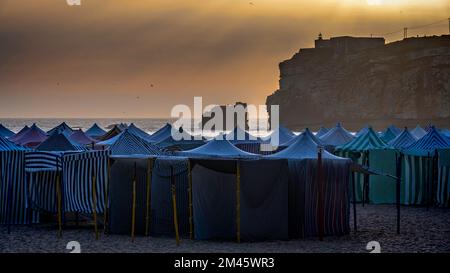 Puesta de sol sobre las cabañas de playa en la playa de Nazare, Nazare, Leiria, Extremadura, Portugal. Foto de stock