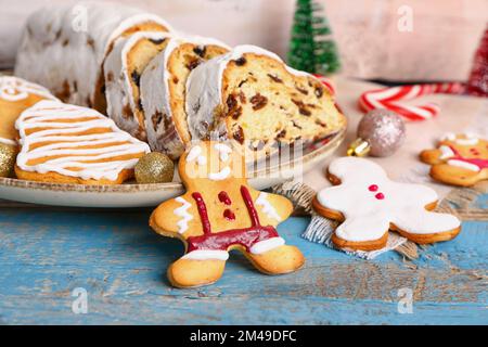 Plato con sabroso stollen de Navidad, galletas y decoraciones en mesa de madera de color, primer plano Foto de stock