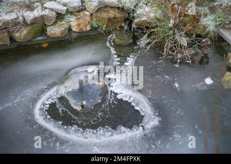 Un estanque de jardín cubierto de hielo con un agujero para la fuente de agua, escena de los inviernos Foto de stock