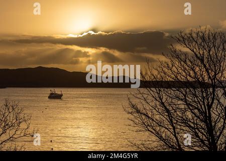 Schull, West Cork, Irlanda. 21st de diciembre de 2022. El sol sale de detrás de las nubes sobre el arrastrero de pesca amarrado 'Laetitia' en Schull Harbour en el día más corto del año. Crédito: AG News/Alamy Live News Foto de stock