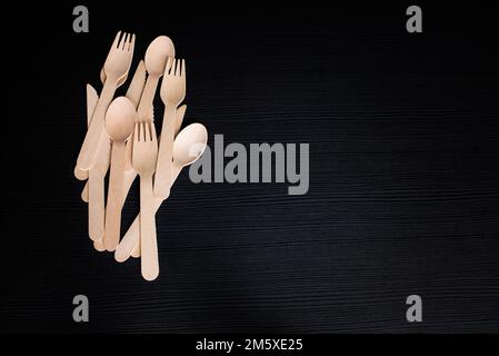 cucharas de madera desechables ecológicas, tenedores y cuchillos sobre un fondo oscuro Foto de stock