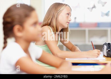 Prestar atención en una lección. Chica joven tomando notas en clase con compañero de clase borroso en primer plano - copyspace. Foto de stock