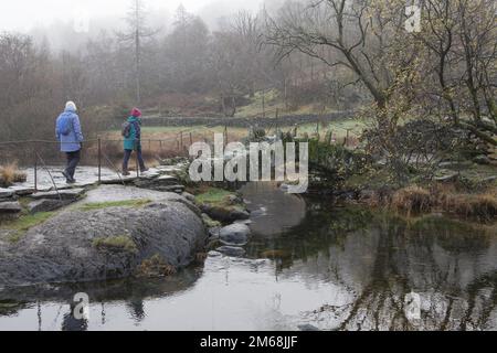 Caminantes cruzar el puente del río Slater & Brathey en Little Langdale, Lake District, Inglaterra Foto de stock