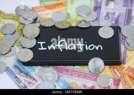 Una rupia y monedas de Sri Lanka alrededor de un texto llamado inflación en la pantalla de un teléfono Foto de stock