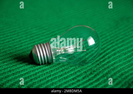 Una lámpara incandescente se encuentra en un tejido de punto verde, ligero Foto de stock