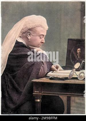 La reina Victoria (1819 - 1901), sentada en su escritorio en la década de 1890s, con una foto de su difunto esposo el príncipe Alberto a su lado. Foto de stock