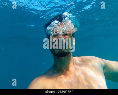 el hombre se está ahogando en un mar azul profundo bajo el agua con una expresión de horror y miedo en su cara Foto de stock