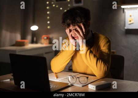 Cándido de joven estudiante masculino trabajo tarde en la noche estrés con el problema de investigación del proyecto en computadora portátil o portátil en la oficina en casa. Quemadura ocupacional Foto de stock