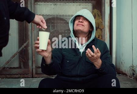 Hombre sin hogar se sienta en los escalones y pide ayuda y dinero. Foto de stock