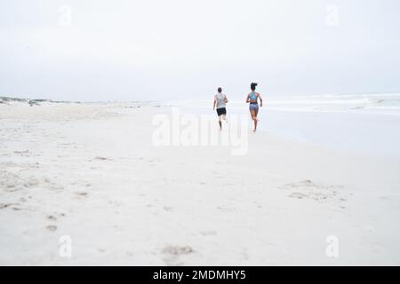 En camino a una mejor salud y bienestar. Foto retrovisora de una joven pareja corriendo a lo largo de la playa juntos. Foto de stock