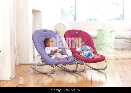 Bebé y niña gemelos sentados en sillas hinchables, vista lateral, 11 semanas