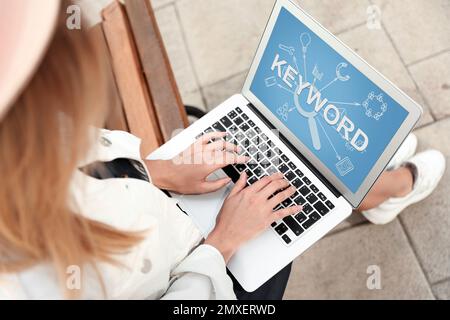 Concepto de investigación de palabras clave. Mujer que trabaja con el ordenador portátil en el banco al aire libre, por encima de la vista Foto de stock