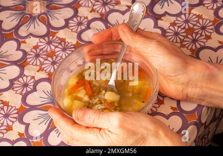 mujer mayor sosteniendo un tazón de sopa en la mesa en la cocina Foto de stock