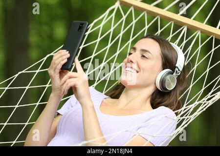 Mujer feliz en la música que escucha de la hamaca en un bosque verde Foto de stock