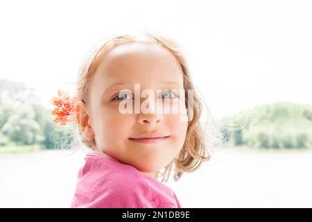 Retrato natural de la belleza de la muchacha joven de una rubia hermosa y sonriente al aire libre con una flor en su pelo.