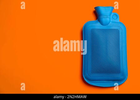 Botella de agua caliente de goma azul sobre fondo naranja, vista superior. Espacio para texto Foto de stock