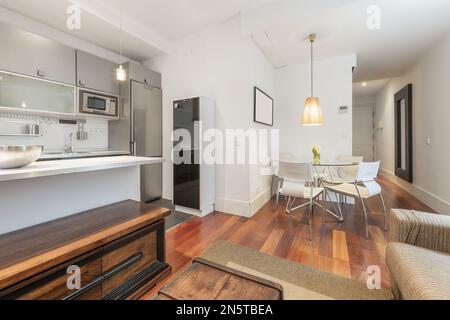 Sala de estar de un apartamento amueblado con una cocina abierta en tonos grises con una mesa de comedor redonda de vidrio Foto de stock