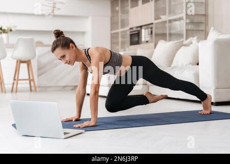 Mujer joven haciendo ejercicio en casa en una sala de estar. lección de  video. mujer joven que repite ejercicios mientras ve la sesión de  entrenamiento en línea. hermosa joven haciendo ejercicio físico