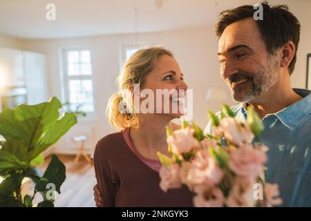Marido feliz sorprendente esposa con flores en casa Foto de stock