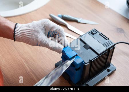 Afilando un cuchillo en un afilador eléctrico en casa. La mano del