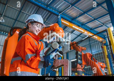 brazo de ensamblaje de robot de control de programación de trabajador de ingeniero inteligente de mujer en la fábrica moderna de la industria del metal Foto de stock