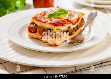 Primer plano de la porción de lasaña en capas con queso ricotta, carne  molida, champiñones, calabacín y salsa de tomate en plato blanco con  tenedor en madera blanca Fotografía de stock - Alamy