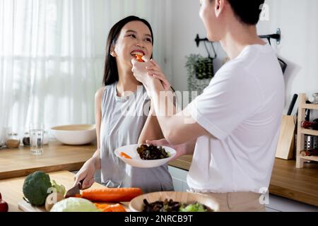 Pareja asiática en relación de amor haciendo una ensalada saludable juntos en la cocina. Sonriente novio feliz y novia disfrutando de la actividad de cocina en el apartamento de casa.
