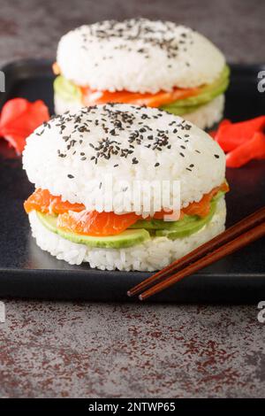 Sándwich de sushi con arroz, salmón, aguacate y sésamo en un plato sobre la mesa. Vertical Foto de stock