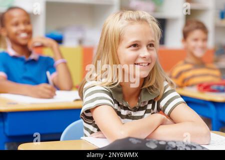 Esta escuela ofrece una educación inspiradora. Chica rubia joven que presta atención en clase y sonríe mientras disfruta de una lección-copyspace. Foto de stock