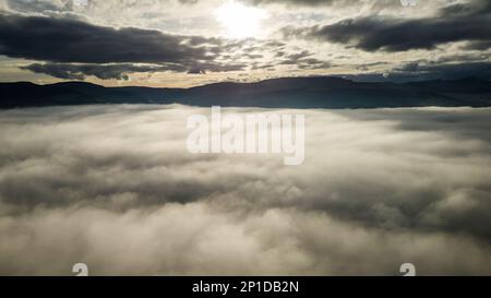 Vista aérea de la puesta de sol sobre un banco de niebla con montañas distantes Foto de stock