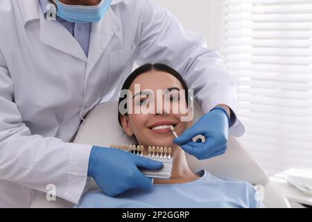 Dentista que comprueba el color de los dientes de la mujer joven en la clínica Foto de stock