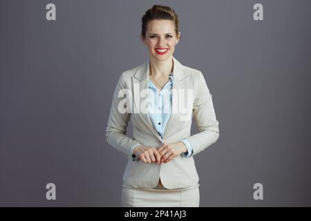 mujer sonriente de mediana edad del dueño de la pequeña empresa en un traje ligero del negocio aislado en gris. Foto de stock