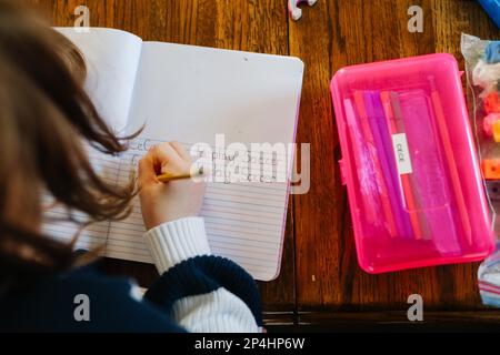 Hija escribiendo palabras junto a la caja de lápiz rosa Foto de stock