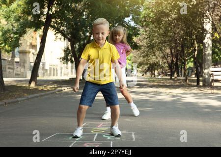 Niños pequeños jugando hopscotch dibujado con tiza en asfalto al aire libre Foto de stock