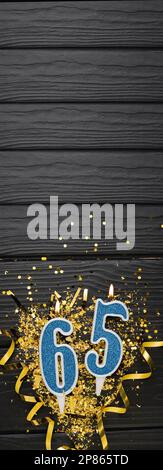 Vela azul de la celebración del número 65 y confeti de oro en fondo de madera oscura. 65th tarjeta de cumpleaños. Aniversario y concepto de cumpleaños. Banner vertical. Foto de stock