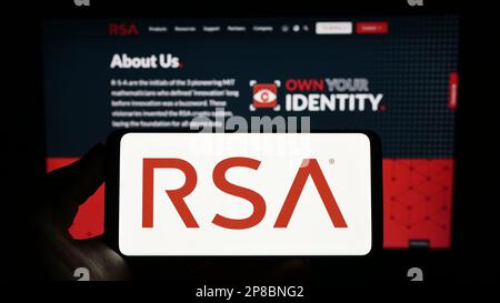 Persona que sostiene el teléfono móvil con el logotipo de la compañía estadounidense RSA Security LLC en la pantalla frente a la página web del negocio. Enfoque en la pantalla del teléfono. Foto de stock