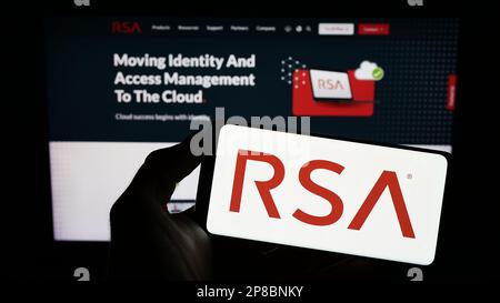 Persona que sostiene el teléfono inteligente con el logotipo de la compañía estadounidense RSA Security LLC en la pantalla frente al sitio web. Enfoque en la pantalla del teléfono. Foto de stock