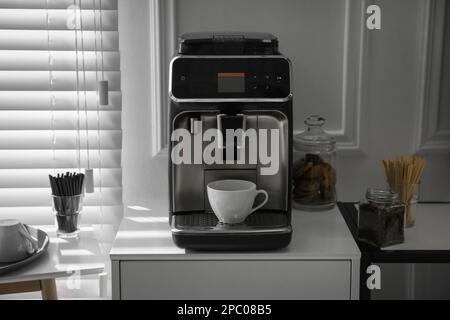 Moderna máquina de café con taza de capuchino en la oficina