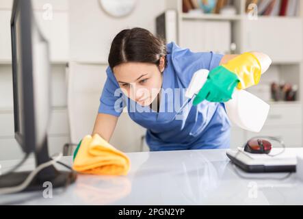 La señora de limpieza de la empresa de limpieza limpia el polvo de la mesa  en la oficina Fotografía de stock - Alamy