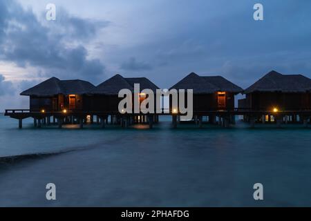 Hermosa vista de las villas de agua en silueta durante la hora azul al atardecer en un complejo de la isla en las Maldivas. Foto de stock