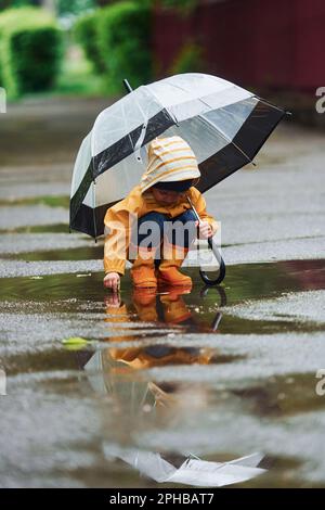 niño con capa impermeable amarilla, botas y paraguas jugando al aire libre  después de la lluvia 15290282 Foto de stock en Vecteezy