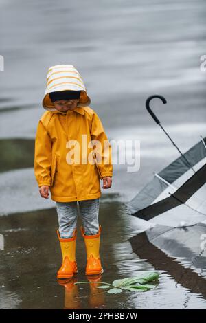 Niño con capa impermeable amarilla y botas jugando al aire libre