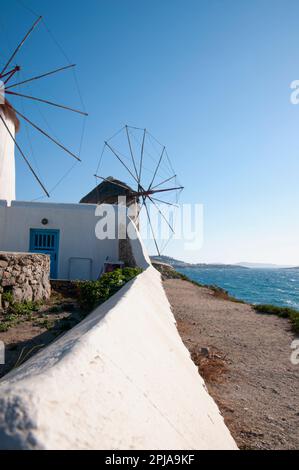 Vista vertical de los molinos de viento blancos en la isla de Mykonos contra el cielo azul. Estos históricos y molinos son un destino turístico para el romántico y ho Foto de stock